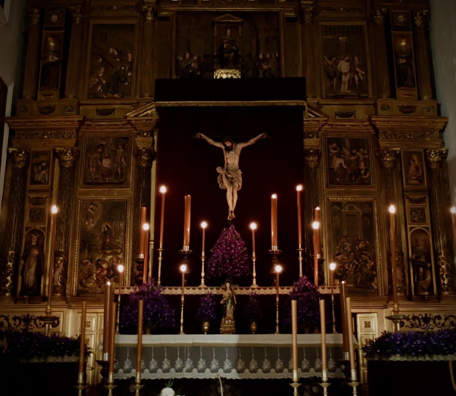 Altar de cultos del Santísimo Cristo de la Misericordia iluminado con cirios y flores moradas